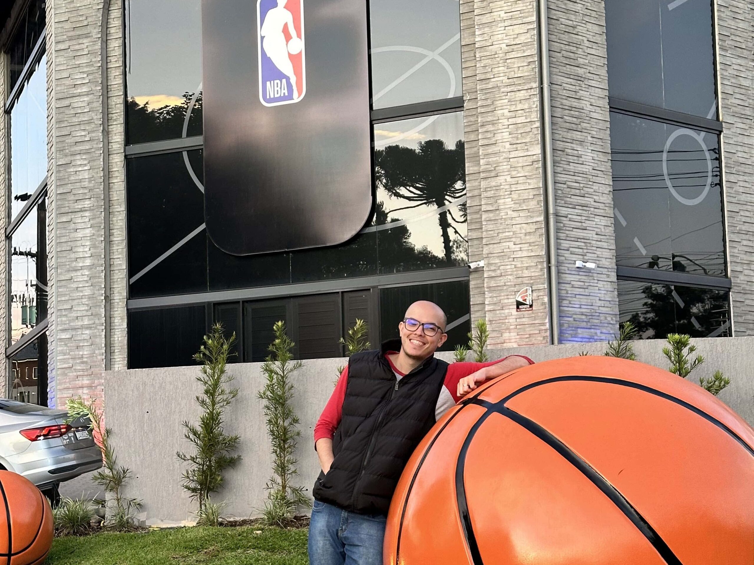 Rafa encostado em uma bola de basquete gigante no NBA Park